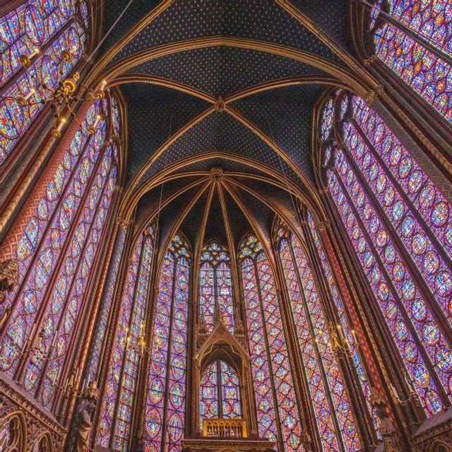 Una vista dal basso dell'interno di una cappella con imponenti e vivaci vetrate colorate e un soffitto a volta scuro decorato con stelle d'oro.