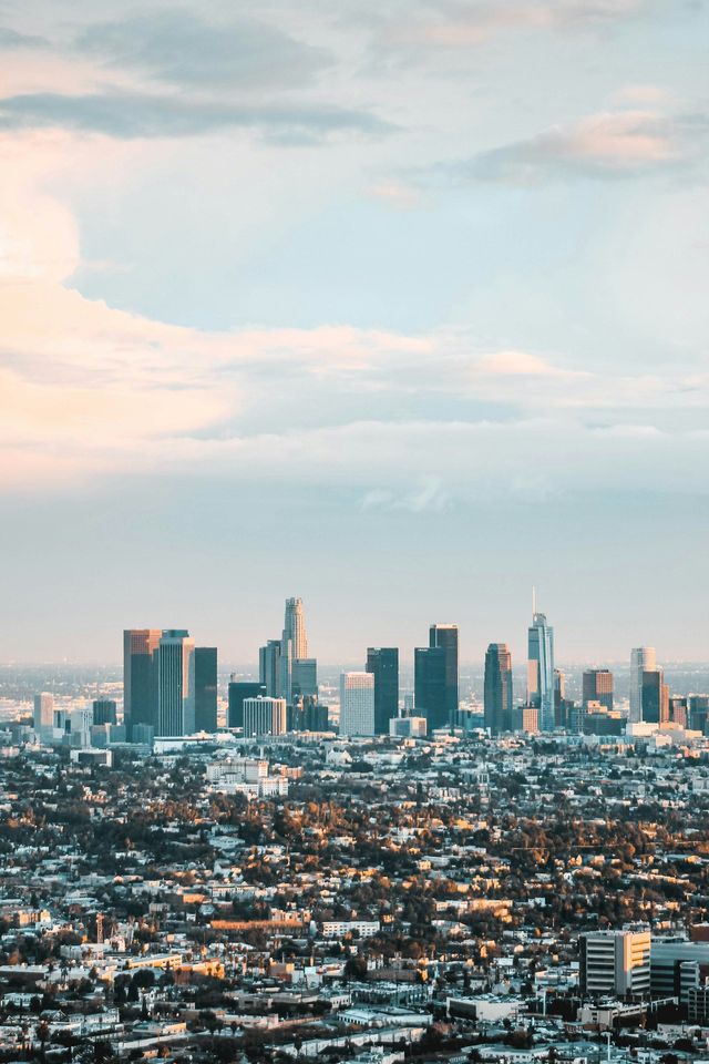 Lo skyline di una città con alti grattacieli si erge sopra un denso paesaggio urbano sotto un cielo morbido e nuvoloso.
