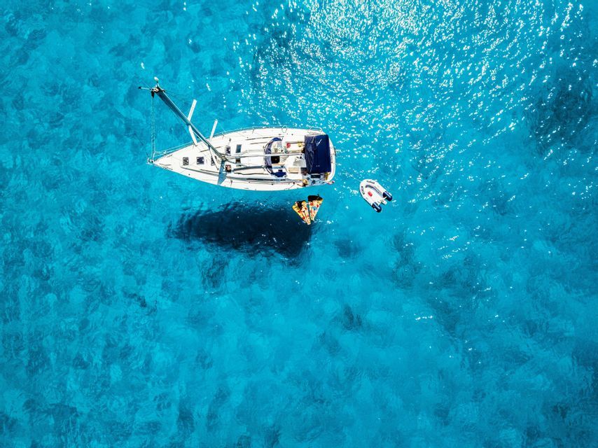 Vista aérea de un velero anclado en agua turquesa, con miembros de un viaje en grupo de WeRoad flotando en una balsa.