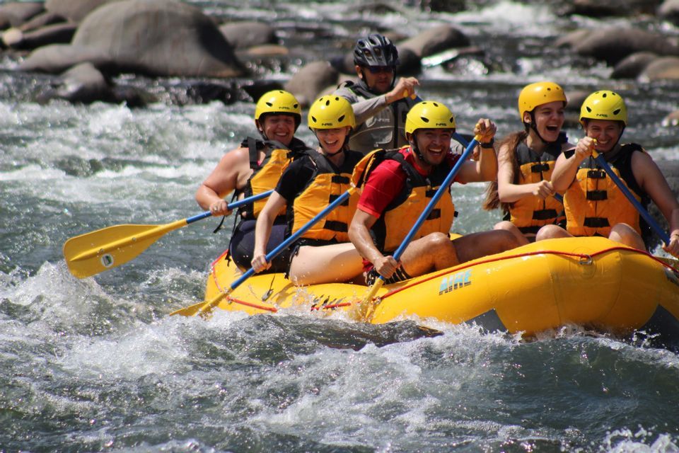 A WeRoad group trip of people in yellow helmets smiling while white-water rafting in an inflatable raft on a rushing river.