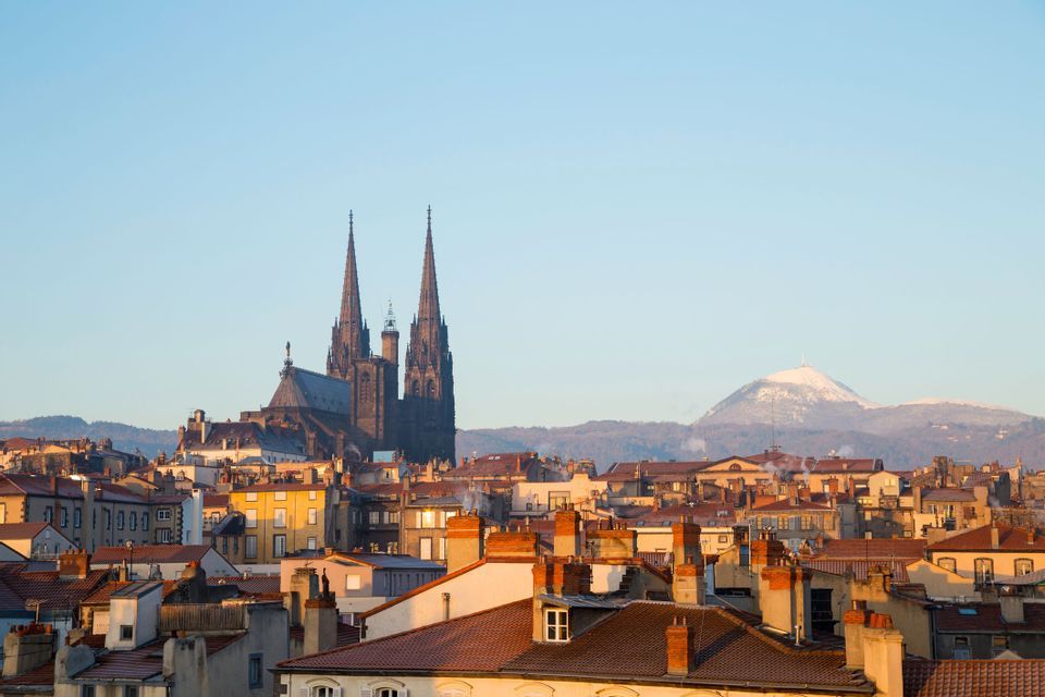 Une cathédrale gothique aux deux flèches s'élève au-dessus des toits de tuiles d'une ville, avec une montagne enneigée au loin.