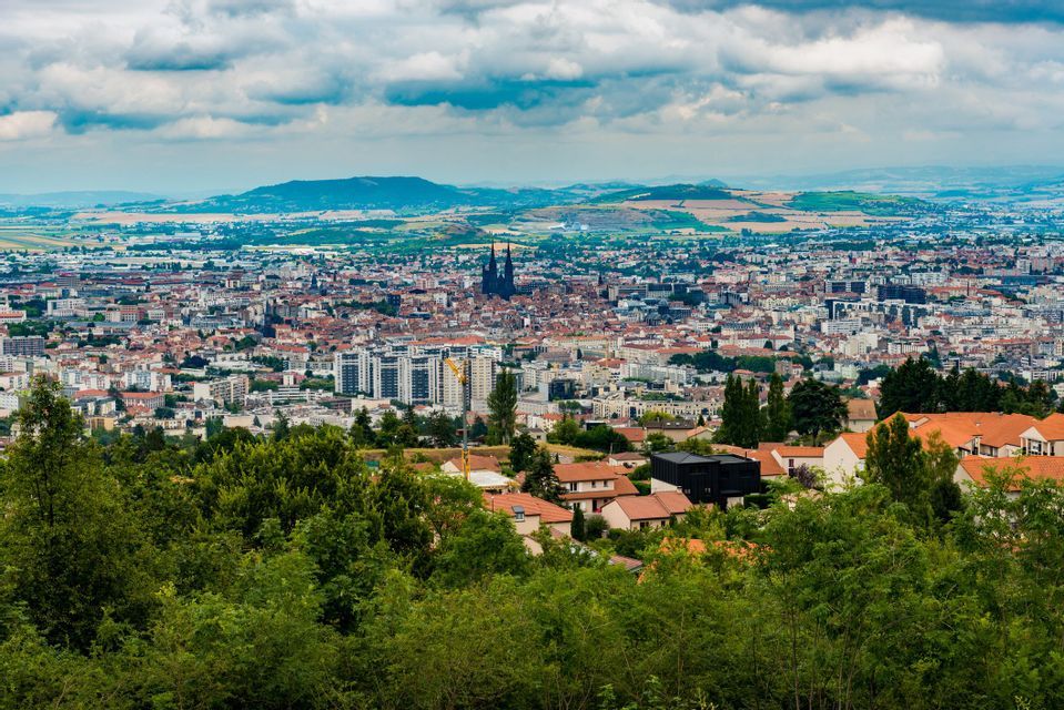 Vue plongeante d'un paysage urbain avec une cathédrale proéminente à deux flèches, vue au-dessus de cimes d'arbres verts sous un ciel nuageux.