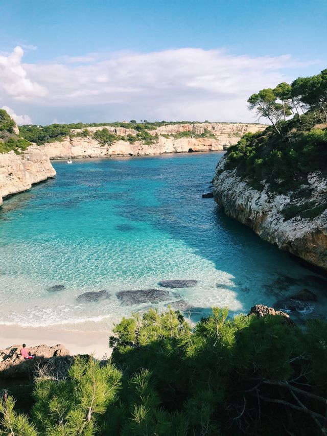 Ein Blick von oben auf eine abgelegene Bucht mit klarem türkisfarbenem Wasser, einem kleinen Sandstrand und felsigen Klippen mit Bäumen.