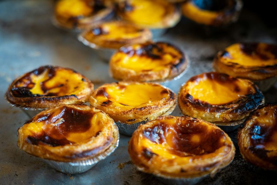 Primo piano di alcuni pastéis de nata con croste sfogliate e caramellate e crema gialla su un vassoio di metallo.