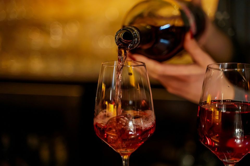 Primo piano di vino rosato versato da una bottiglia in un calice su uno sfondo caldo con effetto bokeh.