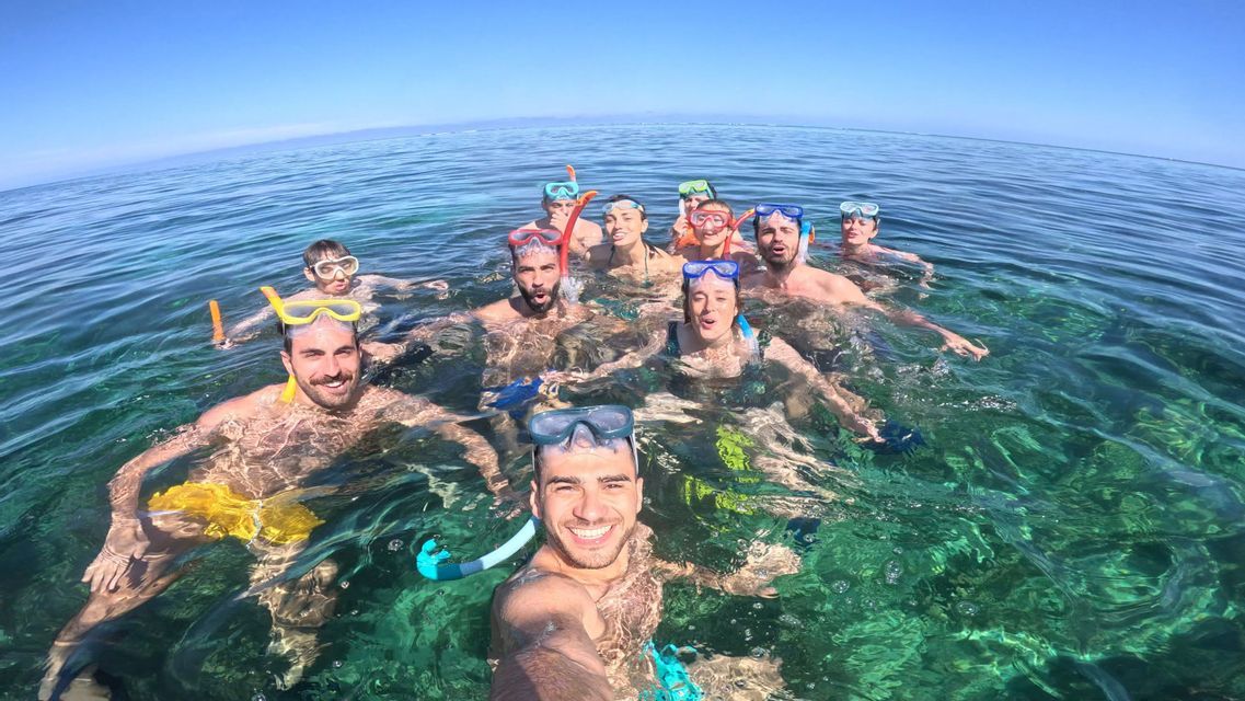 Un groupe WeRoad en voyage, équipé de masques et tubas, sourit pour un selfie en nageant dans une eau turquoise cristalline.