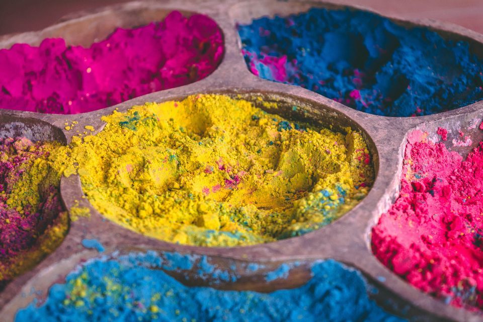 Un primer plano de una bandeja de madera con varias secciones llenas de polvos vibrantes amarillos, magenta y azules.