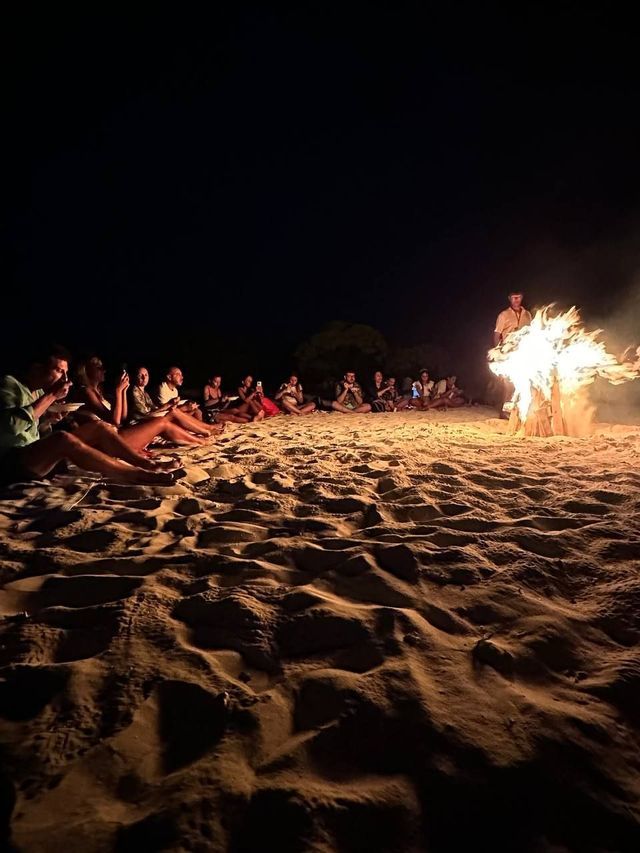 Un viaggio di gruppo WeRoad su una spiaggia sabbiosa di notte, riuniti in cerchio attorno a un grande falò.