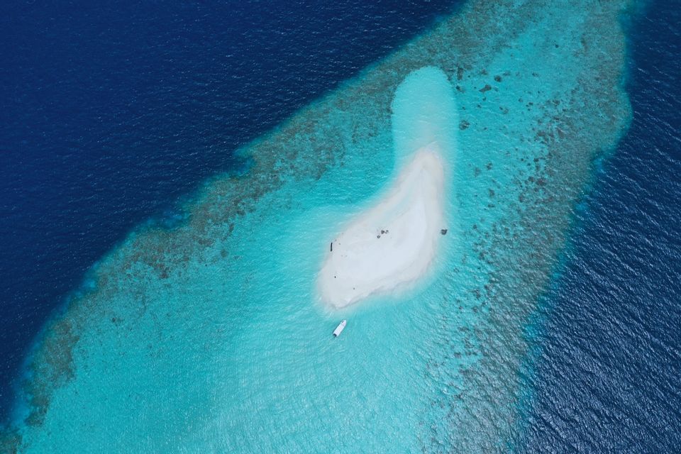 Aerial view of a white sandbar and a small boat in a turquoise lagoon next to the deep blue ocean.