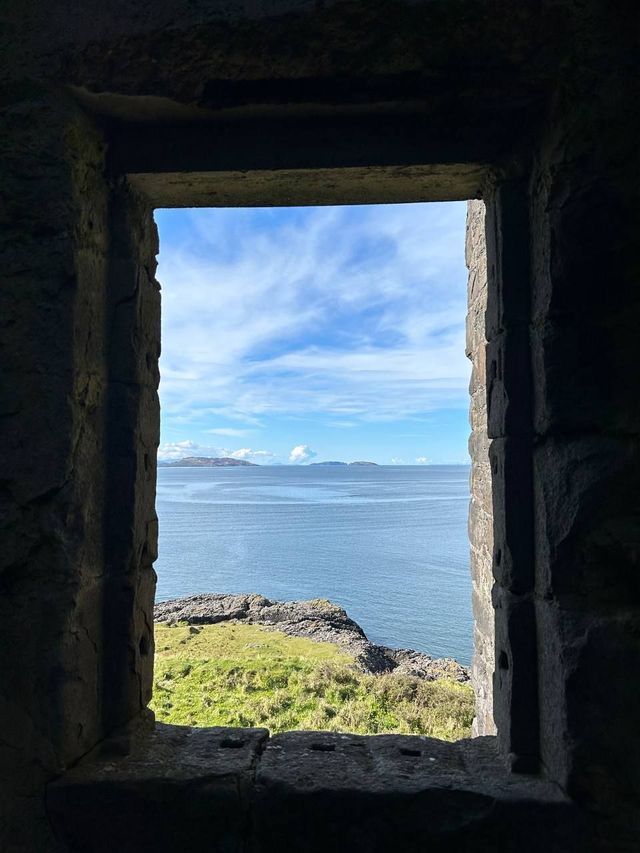 A view of the sea, a green coast, and distant islands as seen from inside through a stone window.