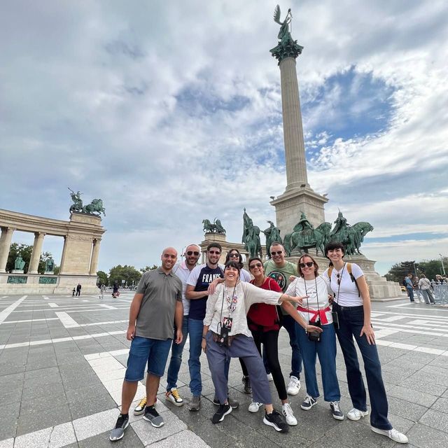 Ein Gruppenreisender von WeRoad posiert auf einem großen Stadtplatz vor einem hohen Denkmal mit Statuen