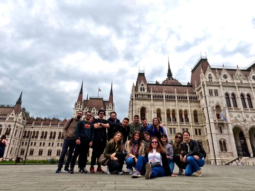 Eine WeRoad-Gruppe posiert unter bewölktem Himmel auf einem Platz vor einem reich verzierten historischen Gebäude für ein Foto.