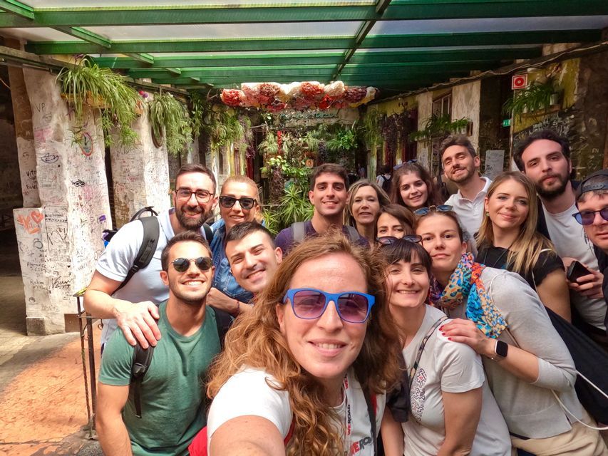 Eine lächelnde WeRoad-Gruppe posiert für ein Selfie in einem engen Innenhof, der mit Hängepflanzen und Graffiti dekoriert ist.