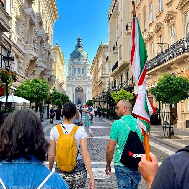 Eine WeRoad-Gruppe geht unter einem klaren, blauen Himmel eine breite Stadtstraße entlang auf eine große Basilika mit Kuppel zu.