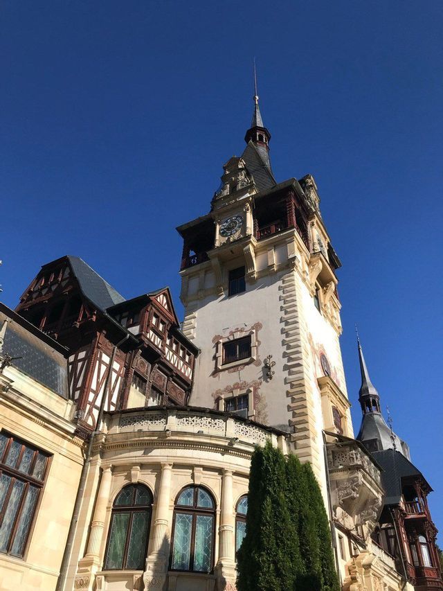 A low-angle view of an ornate castle's clock tower with spires and timber-framed architecture against a clear blue sky.