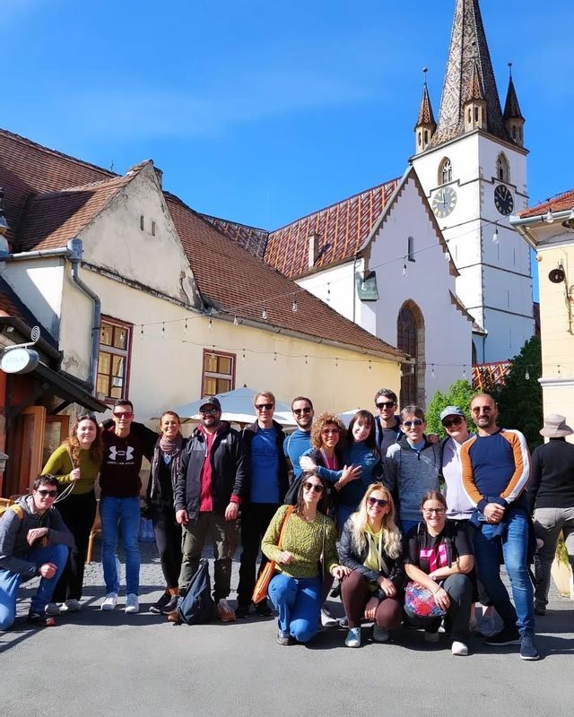 Un gruppo WeRoad in viaggio si ferma per una foto in una piazza assolata, con una chiesa bianca sullo sfondo.