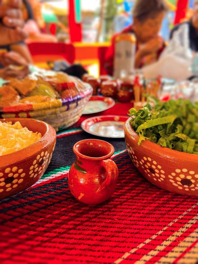Primer plano de una comida con cuencos de terracota y una pequeña jarra roja sobre un mantel colorido y tejido.