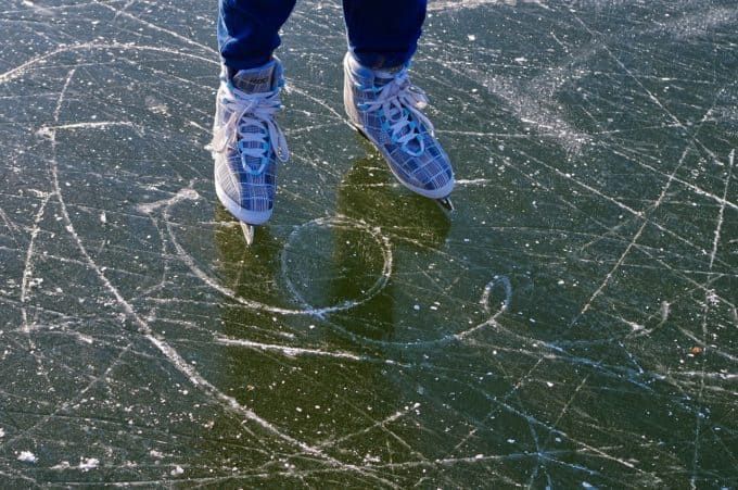 Una persona con pattini da ghiaccio decorati si trova su una superficie di ghiaccio scura coperta da graffi e segni.