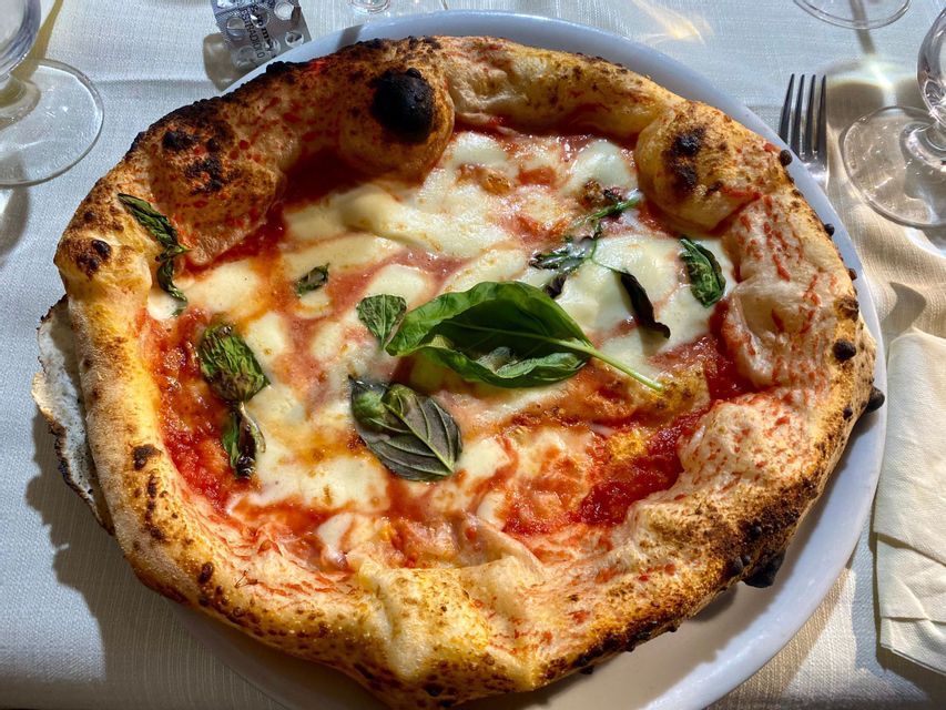 Eine neapolitanische Pizza Margherita mit verkohltem Rand, geschmolzenem Mozzarella und frischem Basilikum auf einem weißen Teller.