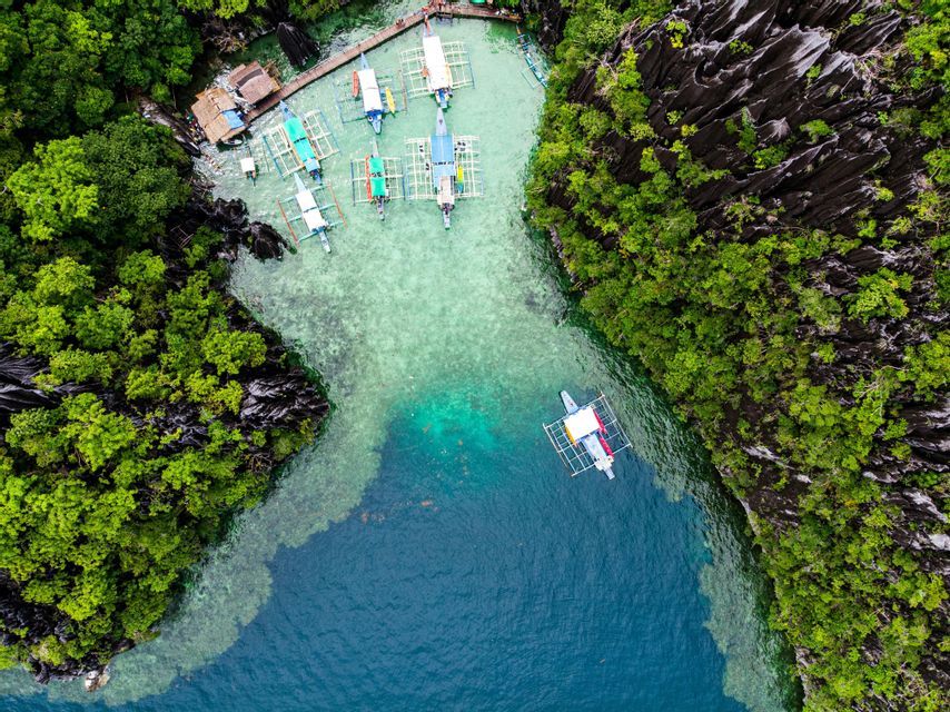 Vista aerea di piroghe tradizionali in una laguna turchese circondata da scogliere rocciose e lussureggianti