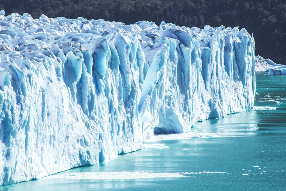Primo piano di una grande parete glaciale con cime frastagliate che scendono in acque calme e turchesi.