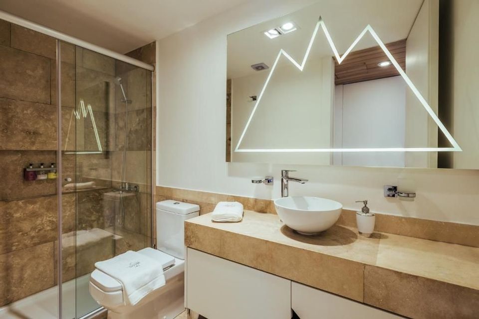 Un bagno moderno con mobile lavabo in pietra, lavabo a ciotola e un grande specchio con design montano illuminato.