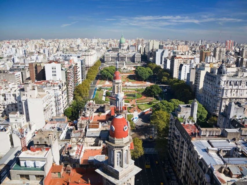 Una vista aerea di una vasta città con un ampio viale alberato che conduce a un grande edificio a cupola sotto un cielo azzurro.