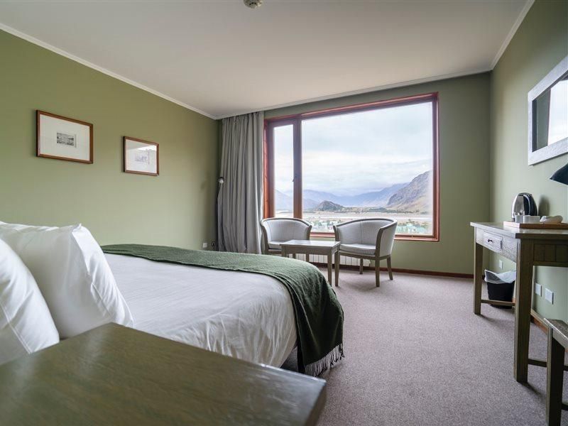 Una camera d'albergo con pareti verde salvia e un'ampia finestra che si affaccia su una pittoresca valle di montagna.