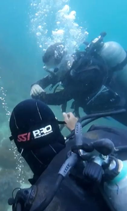 Una vista in prima persona di un viaggio di gruppo WeRoad per immersioni subacquee, con un altro subacqueo e bolle visibili nell'acqua limpida e blu.
