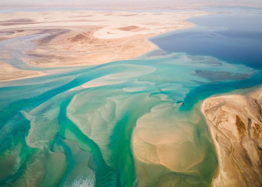 Una vista aerea di una costa desertica dove acque turchesi e poco profonde scorrono su intricati banchi di sabbia