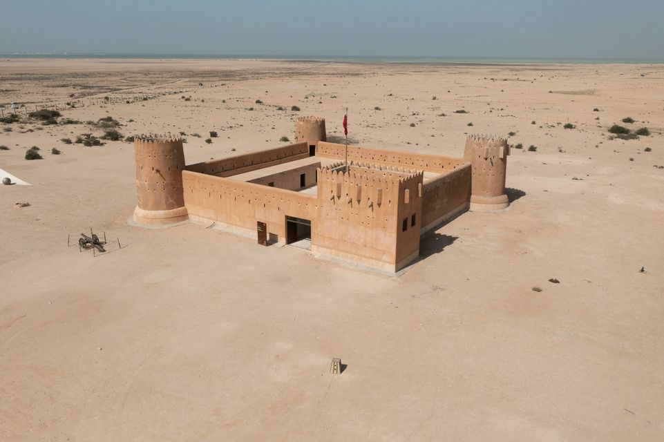 Veduta aerea di un forte color sabbia con quattro torri in un vasto deserto, con il mare visibile all'orizzonte.