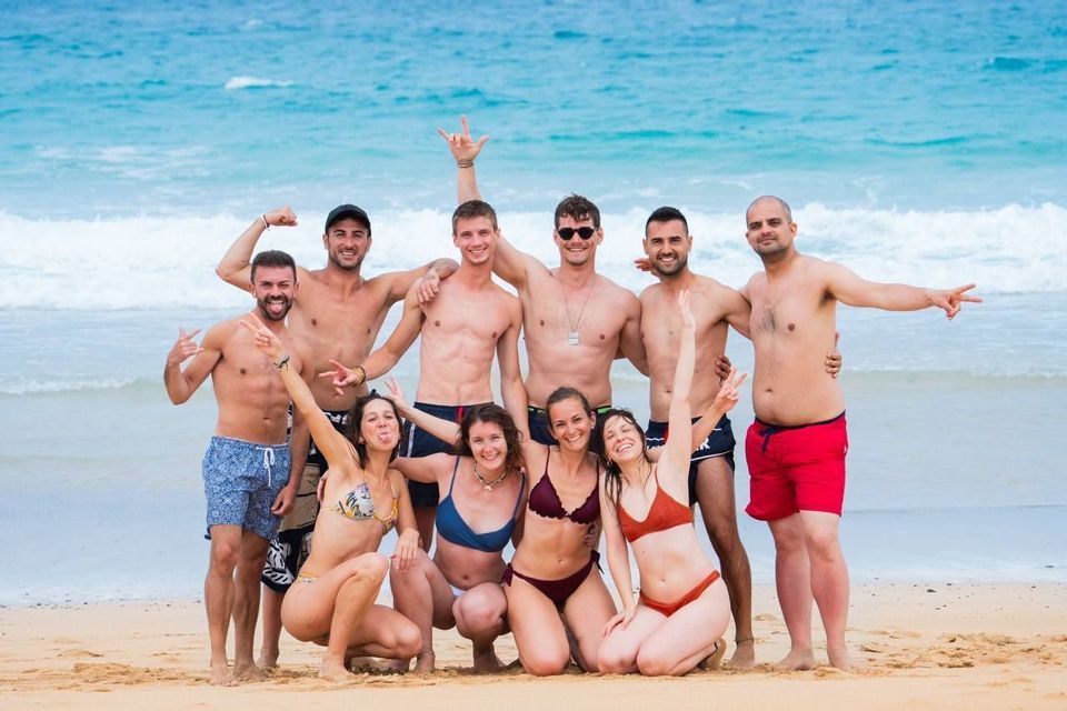 Un viaggio di gruppo WeRoad di uomini e donne in costume da bagno che posano e sorridono per una foto su una spiaggia sabbiosa.