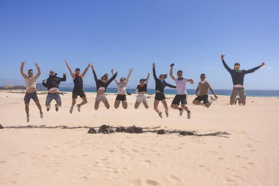 Un viaje en grupo de WeRoad de nueve personas saltando en el aire en una playa de arena con el océano de fondo.