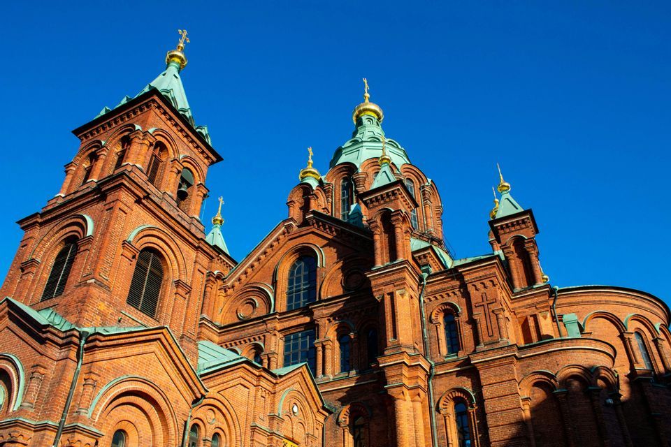 Una sontuosa cattedrale in mattoni rossi con cupole verdi e croci dorate, vista dal basso su uno sfondo di cielo azzurro e limpido.