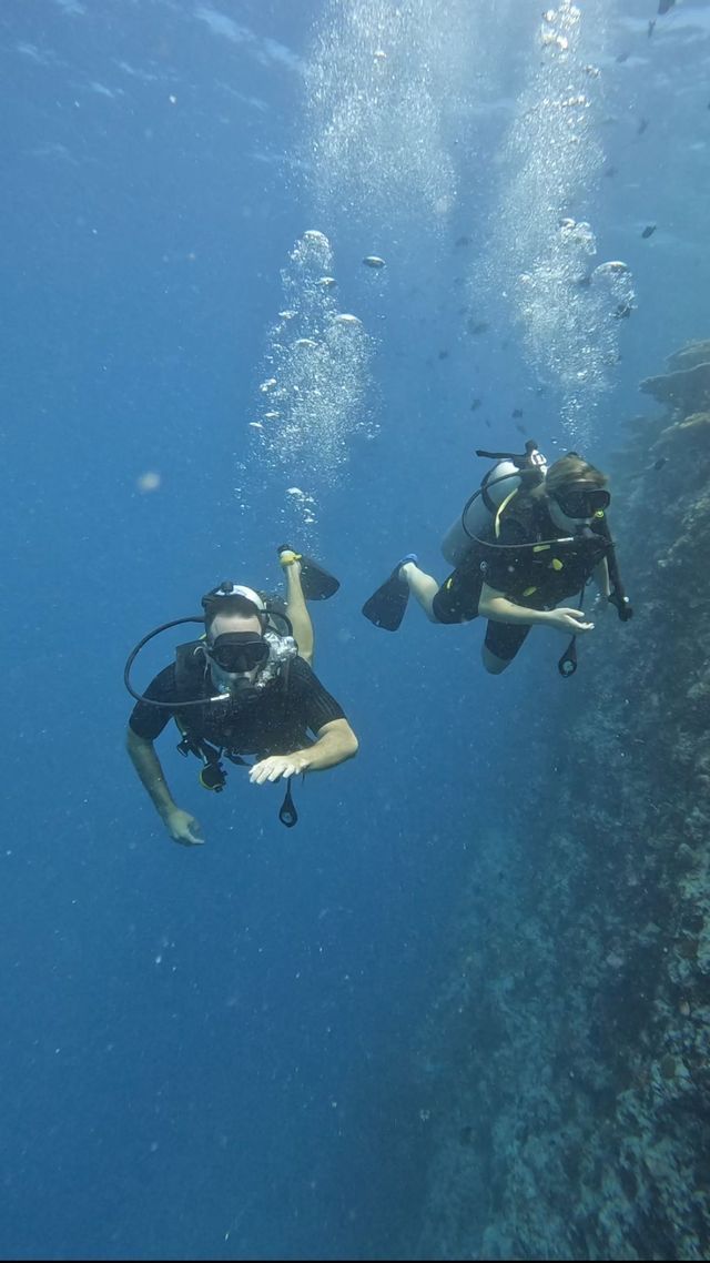 Dos personas en un viaje grupal de WeRoad bucean en aguas azul profundo con burbujas que suben a la superficie.