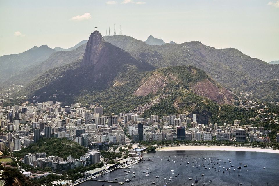 Una vista aerea di una città costiera e una baia con barche, con uno sfondo di montagne verdi sormontate da una grande statua