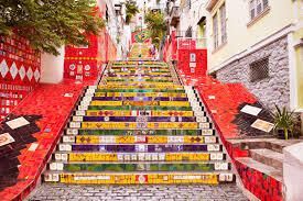 Una lunga e ripida scalinata esterna decorata con piastrelle a mosaico colorate, affiancata da edifici con muri in tegole rosse.