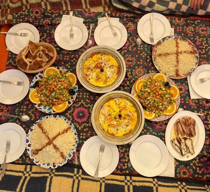 Vista dall'alto di un pasto tradizionale imbandito su un tappeto colorato a motivi, con couscous, insalata e tajine.