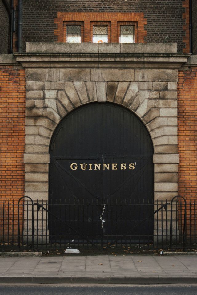 Un grande cancello ad arco nero con la scritta 'GUINNESS' in lettere dorate, inserito nella facciata di un edificio in pietra e mattoni.