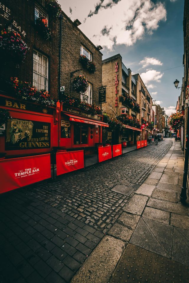 La facciata rosso brillante del pub The Temple Bar che costeggia una stretta via acciottolata sotto un cielo parzialmente nuvoloso.