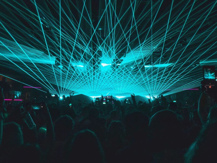 A crowd of people silhouetted against a network of bright blue lasers at a concert.