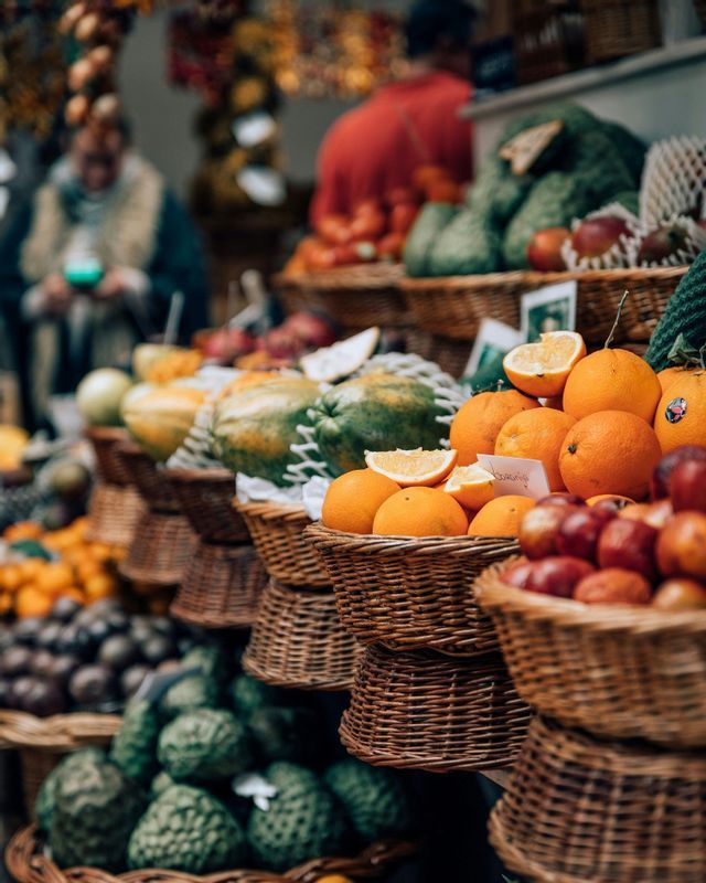 Una varietà di frutta fresca, tra cui arance, mele e cherimoya, è esposta in cesti intrecciati presso una bancarella di un mercato all'aperto