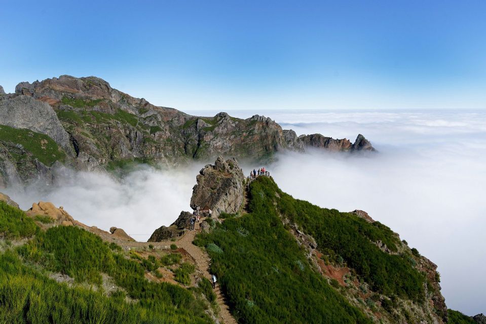 Un viaggio di gruppo WeRoad si trova su uno stretto sentiero di cresta montano, affacciato su un paesaggio di vette che si ergono sopra un mare di nuvole.