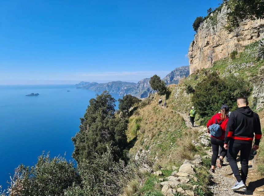 Un viaggio di gruppo WeRoad che percorre uno stretto sentiero su una scogliera erbosa, affacciato sul mare blu e sulla costa distante.