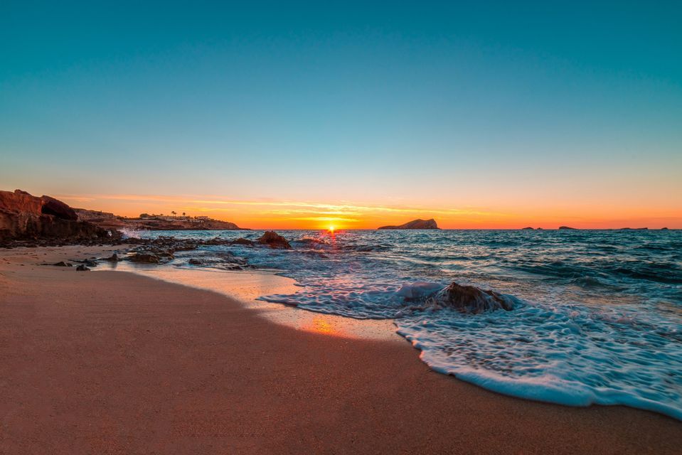 Un tramonto vibrante sull'oceano con onde che lambiscono una spiaggia sabbiosa accanto a una costa rocciosa.