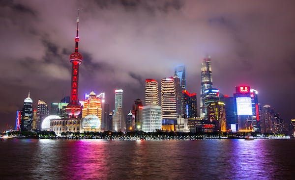 Una luminosa skyline notturna, con un'alta torre rossa e grattacieli che si riflettono nell'acqua.