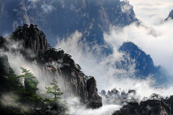 Vette rocciose coperte di pini emergono da uno spesso strato di nebbia e nuvole.