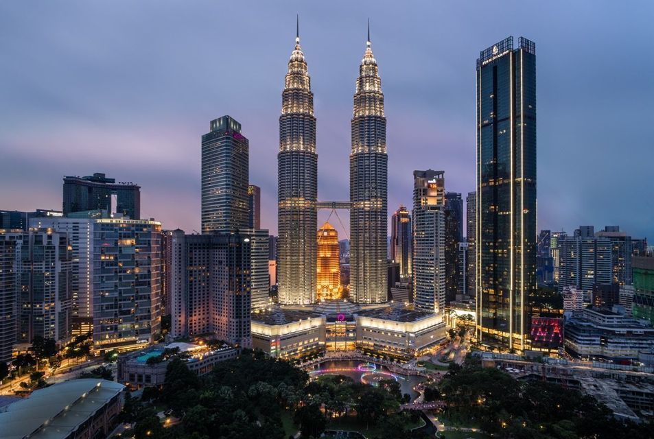 Due grattacieli gemelli illuminati con un ponte aereo di collegamento si ergono sopra lo skyline di una città moderna sotto un cielo crepuscolare.