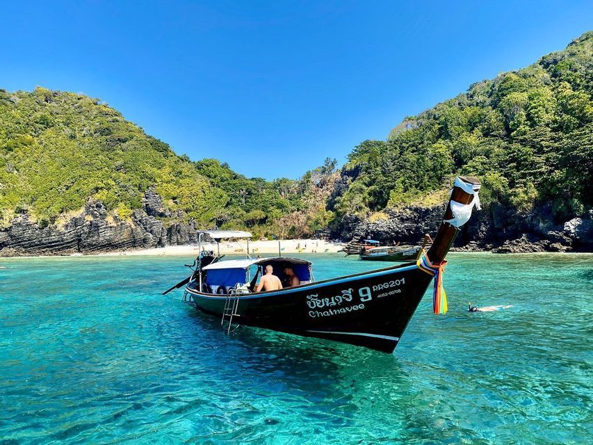 Una tradizionale barca long-tail con a bordo viaggiatori di un gruppo WeRoad galleggia su acque calme e turchesi vicino a un'isola tropicale con spiaggia di sabbia.