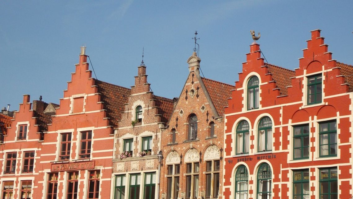 Una fila di colorati edifici in mattoni con distintive facciate a gradoni si staglia contro un cielo azzurro limpido.